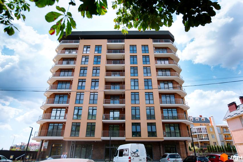 Зовнішній вигляд ЖК SilverPark: багатоповерховий будинок з балконами та великими вікнами на фоні блакитного неба з хмарами.