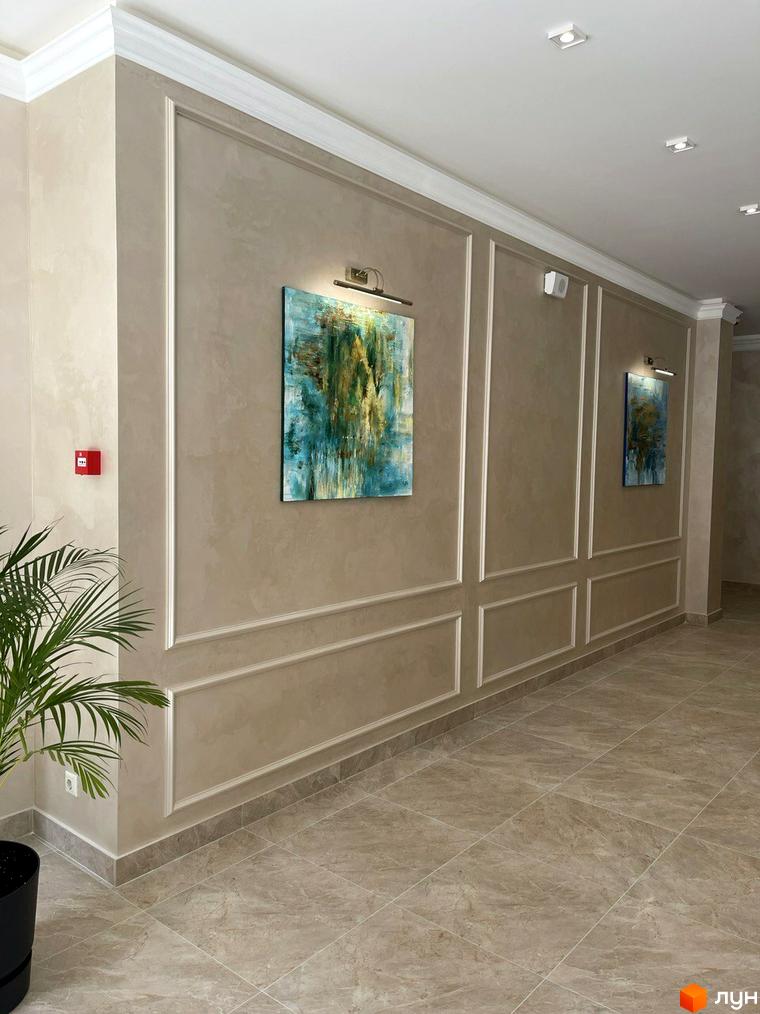 Коридор у ЖК Родос з картинами на стінах, оздоблений декоративними елементами. Підлога викладена плиткою, а стеля має вбудовані світильники.