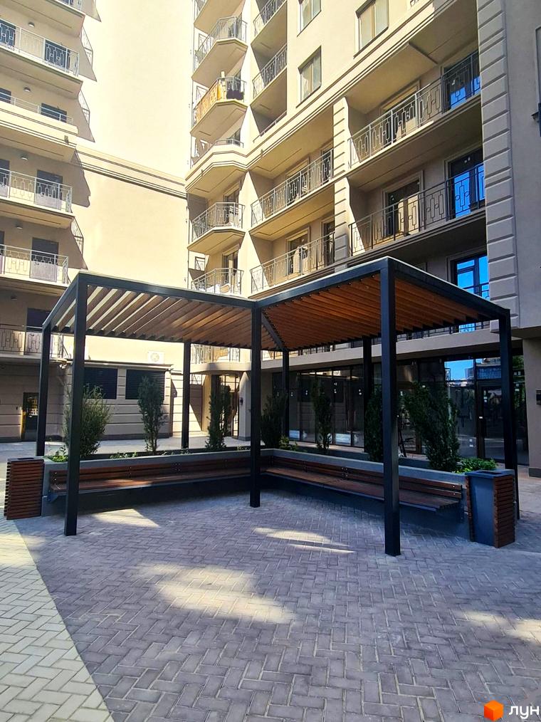 Житловий комплекс Родос з архітектурою у світлих тонах. На території комплексу розташована зона відпочинку з лавками.