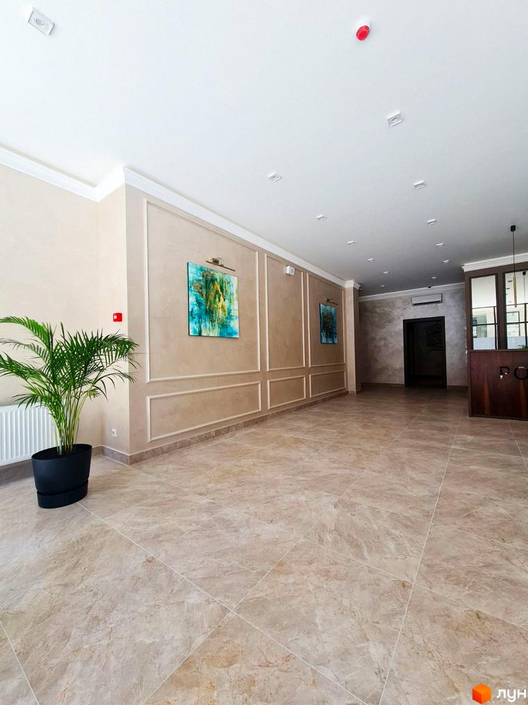 Просторий хол Житлового комплексу Родос з бежевими стінами, плитковою підлогою, рослиною та картинами. Світлий інтер'єр вестибюля.
