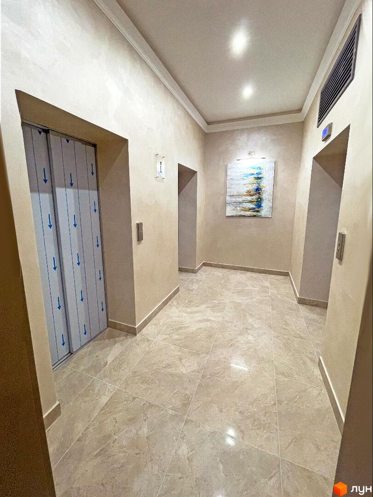 Внутрішній простір Житлового комплексу Родос: світлий коридор з плитковою підлогою, текстурованими стінами та ліфтом.