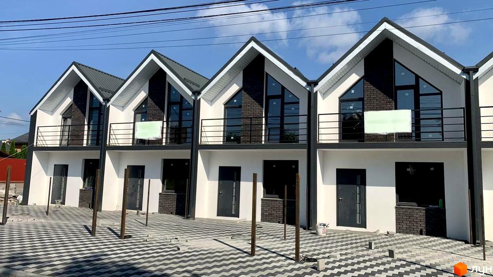 Зображення фасаду таунхаусів в ЖК Vasylkivska з білими стінами, чорними вікнами та балконами. На передньому плані бруківка.