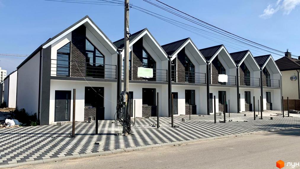 Зовнішній вигляд таунхаусів Vasylkivska з білими фасадами, чорними дахами та терасами. Передня частина з бруківкою.