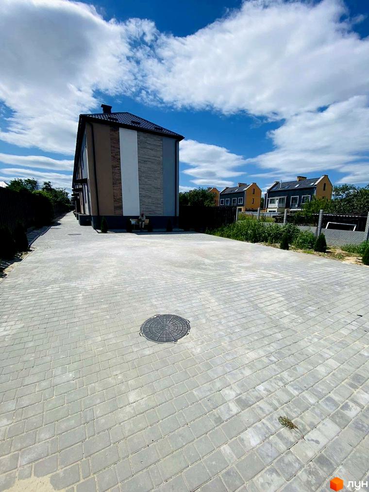 Зовнішній вигляд будинку в житловому комплексі Comfort home з фасадом у світлих тонах та вимощеною прибудинковою територією.