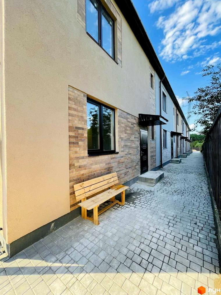 Зовнішній вигляд таунхаусів Comfort home з цегляним фасадом та дерев'яною лавкою біля входу. На території викладена тротуарна плитка.