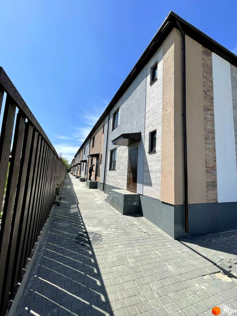 Зображення сторінки житлового комплексу Comfort home. Будинки з сірими, бежевими та білими фасадами. Дорога викладена плиткою, з одного боку дерев'яний паркан.