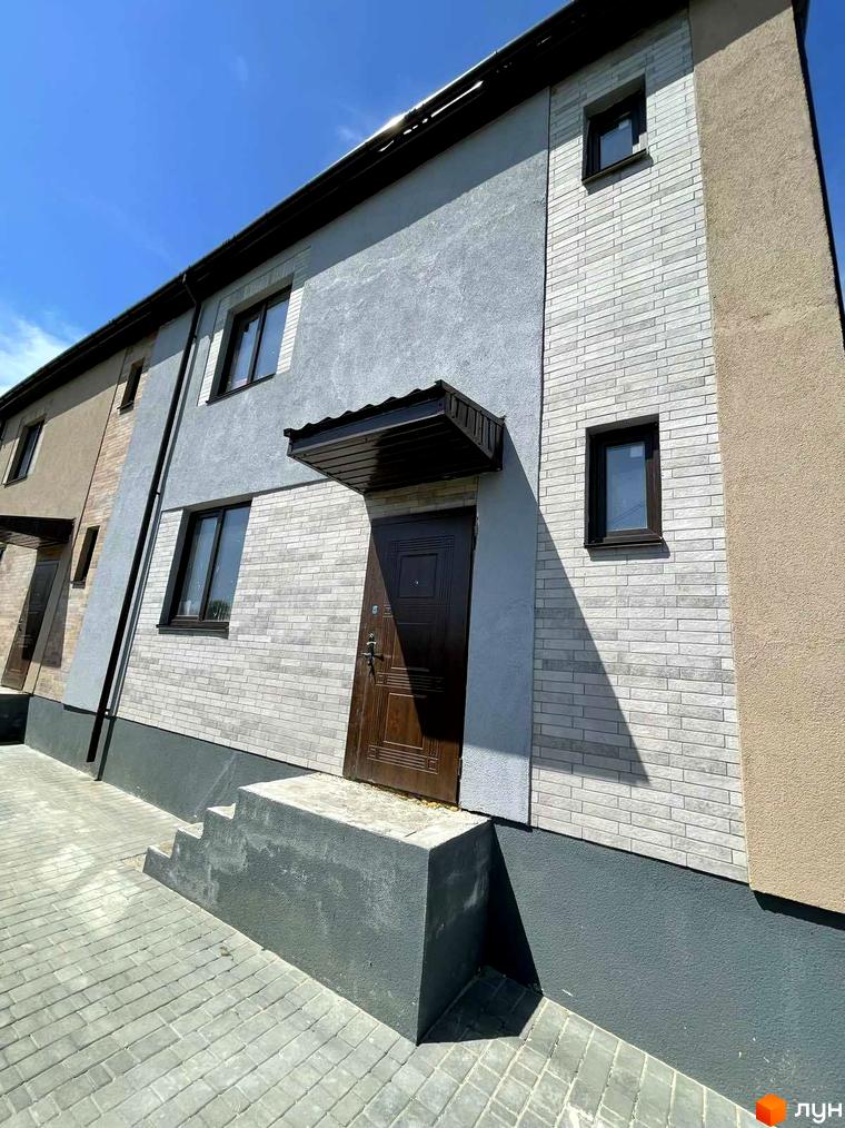 Зовнішній вигляд таунхауса в Comfort home. Фасад будинку з сірою цеглою, коричневі двері та вікна, перед будинком тротуарна плитка.