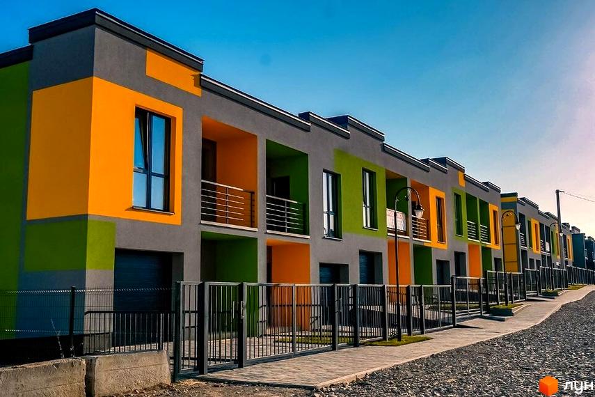 Котеджне містечко КМ Дем’янів лаз: фасади будинків у сірих, жовтих та зелених кольорах, огороджена територія з парканом та воротами.