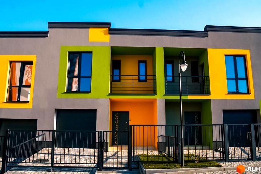 Фасад Котеджного містечка Дем’янів лаз з кольоровими вставками та чорними вікнами. Перед будинками є огорожа та бруківка.