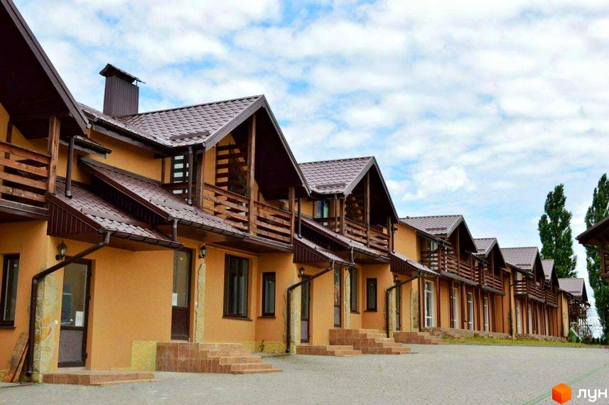 Зображення таунхаусів „Андора“ з коричневими дахами та дерев'яними балконами. Перед будинками викладена тротуарна плитка.