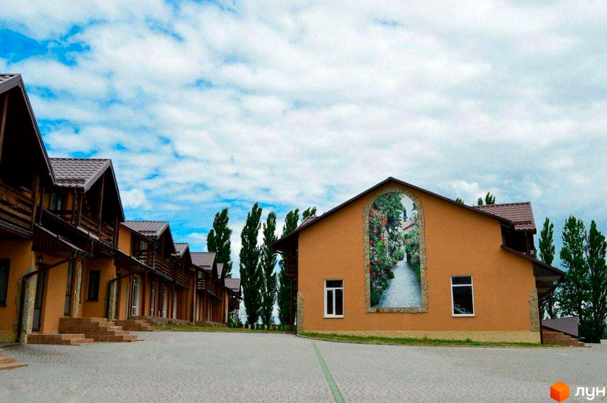 Зовнішній вигляд таунхаусів „Андора“ з коричневими дахами та оздобленими фасадами. На території ростуть високі дерева та є широка пішохідна зона.