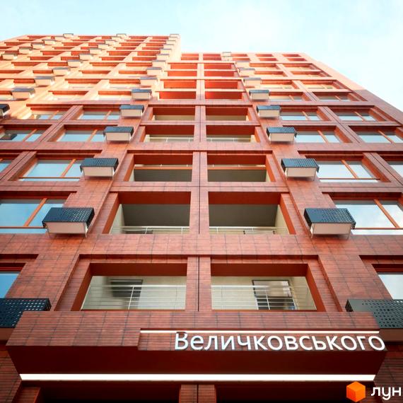 Фасад житлового комплексу на Величковського з червоної цегли, з балконами та кондиціонерами на тлі блакитного неба.