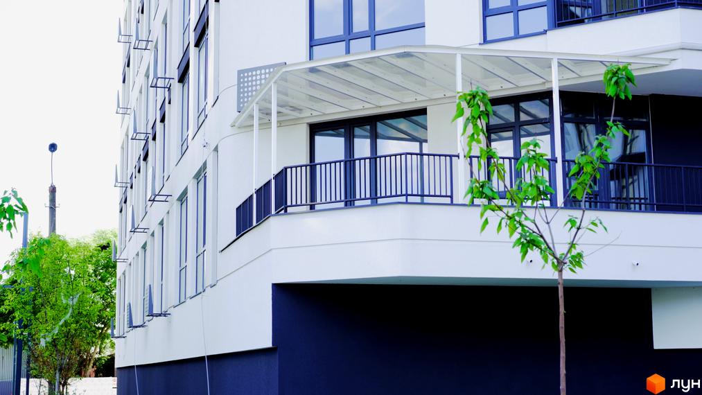 Зовнішній вигляд будинку в Житловому комплексі Лісопарковий. На передньому плані невеличке дерево з зеленим листям.