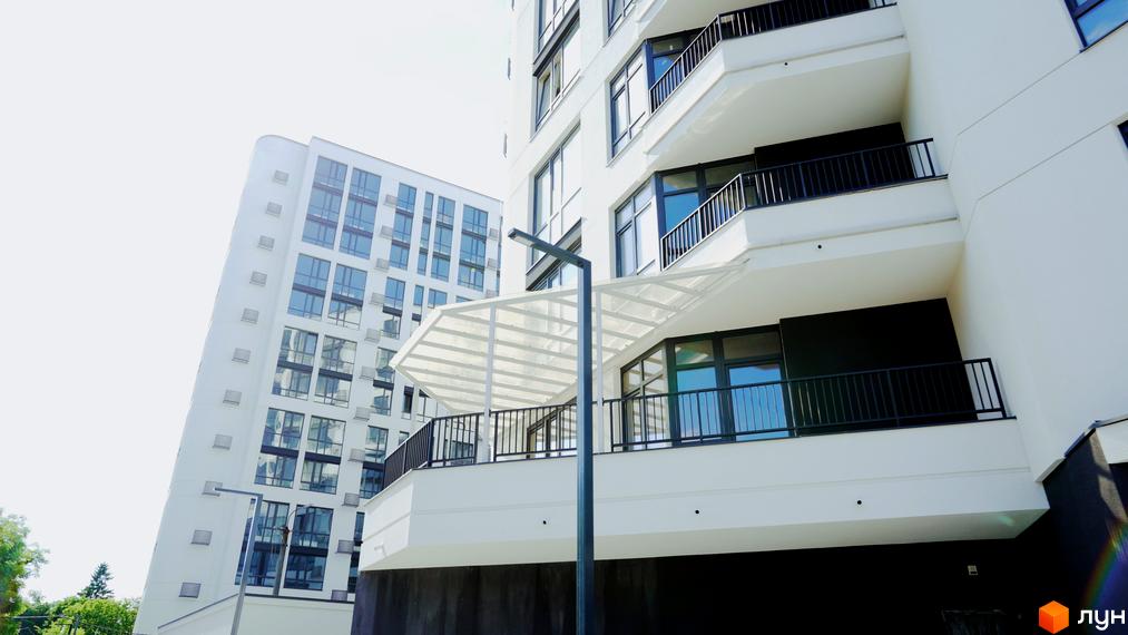 Зовнішній вигляд будинку в Житловому комплексі Лісопарковий з балконами та панорамними вікнами. На передньому плані освітлення.