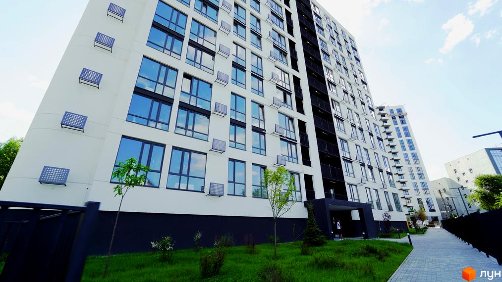 Зображення фасаду багатоповерхового будинку в Житловому комплексі Лісопарковий. Навколо будинку зелена прибудинкова територія.