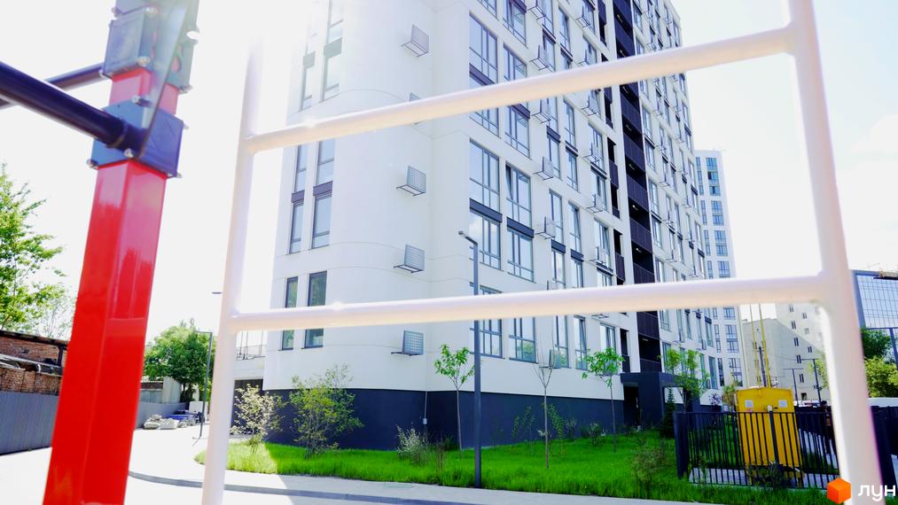 Зображення фасаду багатоповерхового будинку в Житловому комплексі Лісопарковий. На передньому плані дитячий майданчик.