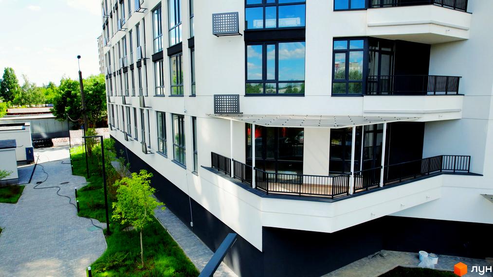 Зображення фасаду будинку Житлового комплексу Лісопарковий. Вигляд на прибудинкову територію з тротуаром та озелененням.