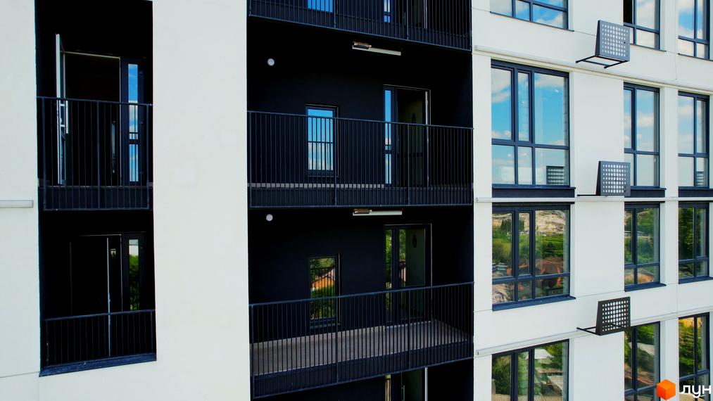 Зовнішній вигляд будівлі Житлового комплексу Лісопарковий з балконами та великими вікнами. Фасад будинку білого та чорного кольору.
