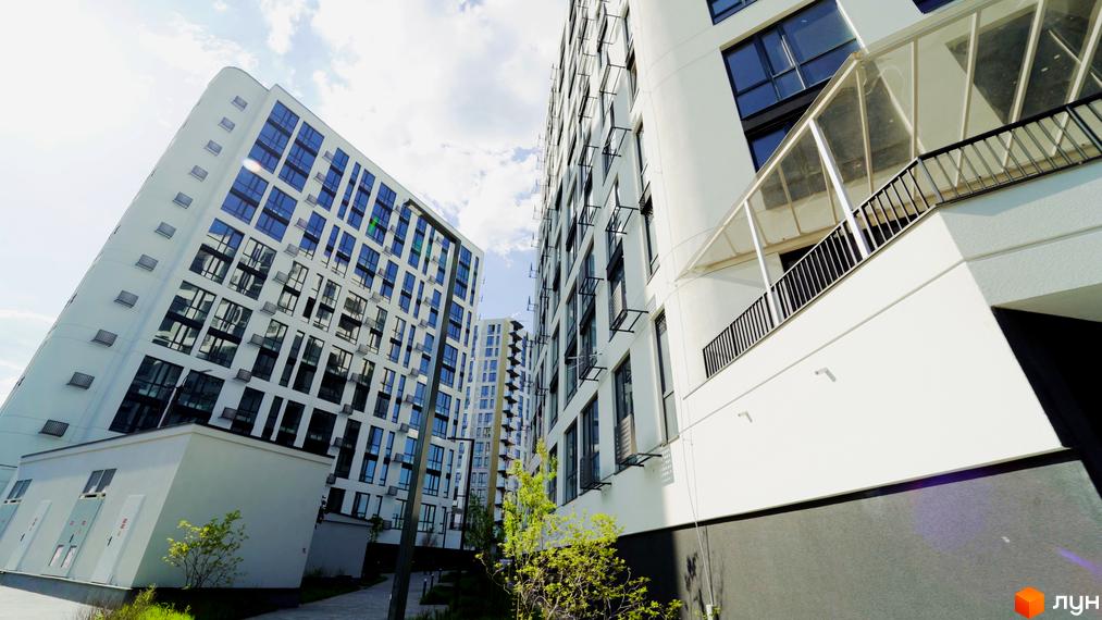 Зображення фасаду багатоповерхового будинку в Житловому комплексі Лісопарковий. Навколо будинку зелені насадження та пішохідні доріжки.