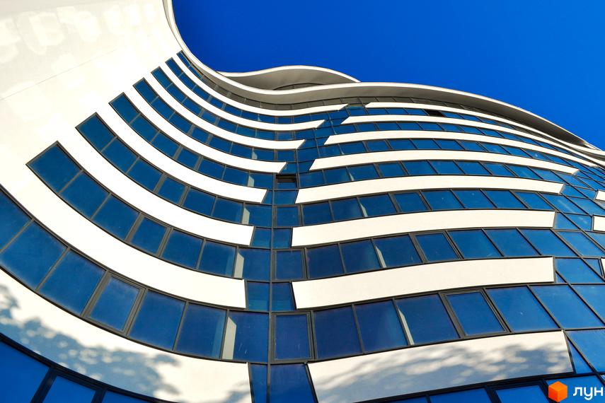 Зображення фасаду Житлового комплексу Parus з великими вікнами. Архітектура будинку з плавними лініями на фоні синього неба.