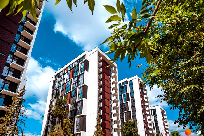 Житловий район Manhattan: новобудови з білими та темними фасадами, численними вікнами та балконами на тлі зелених дерев та блакитного неба.