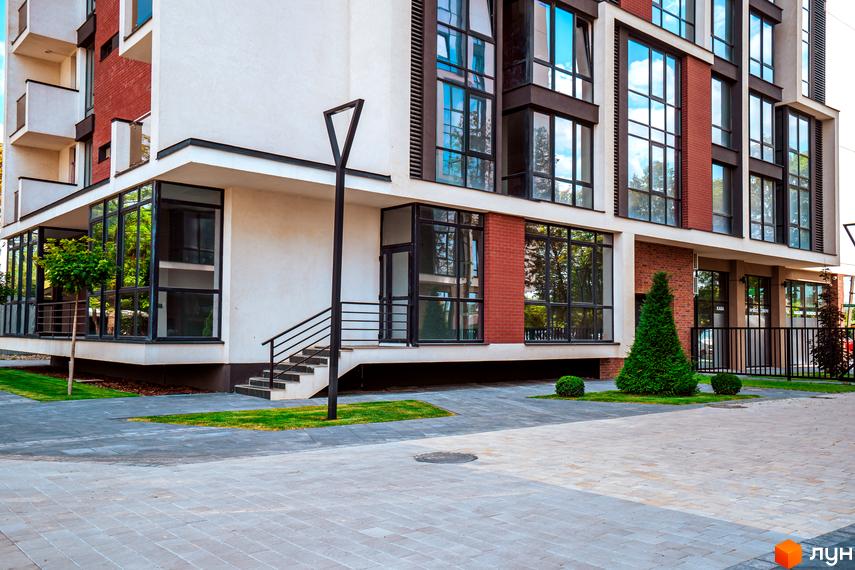 Житловий район Manhattan - сучасна архітектура з великими вікнами та цегляними вставками, доглянута прибудинкова територія з газоном та деревами.