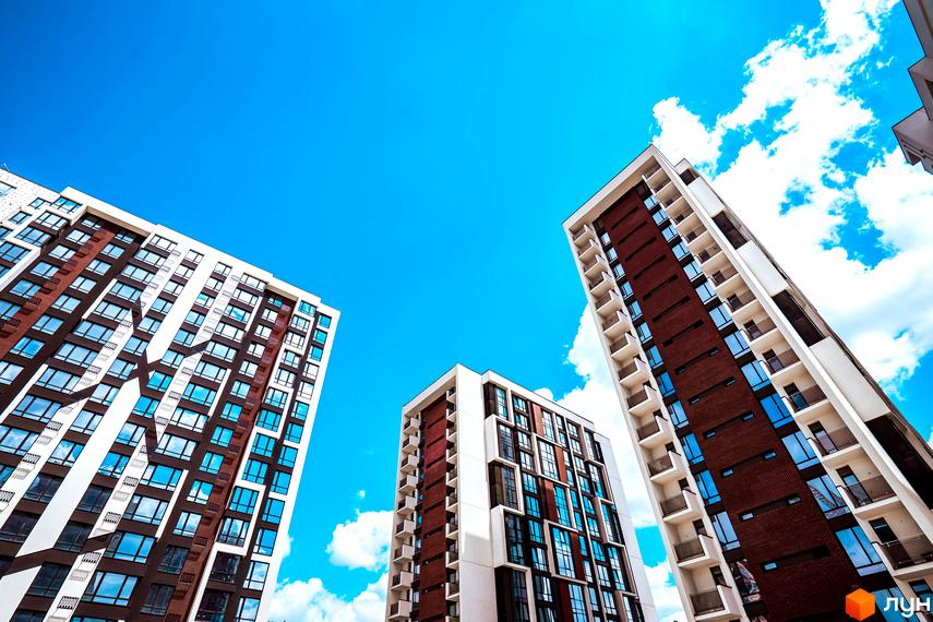 Житловий район Manhattan. Сучасні висотні будинки з цегляним та білим оздобленням фасадів, великою кількістю вікон та балконів на тлі блакитного неба з хмарами.