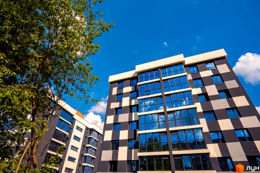 Зовнішній вигляд новобудови ЖК Union з панорамними вікнами та оригінальним фасадом у шаховому порядку. Навколо будівлі зелені дерева під яскравим блакитним небом.