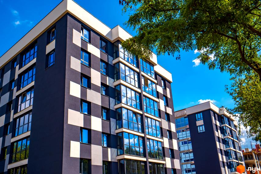 Зовнішній вигляд житлового комплексу Union з темно-сірими та світлими квадратами на фасаді та великими вікнами, що відбивають небо. Навколо зелені дерева та блакитне небо.