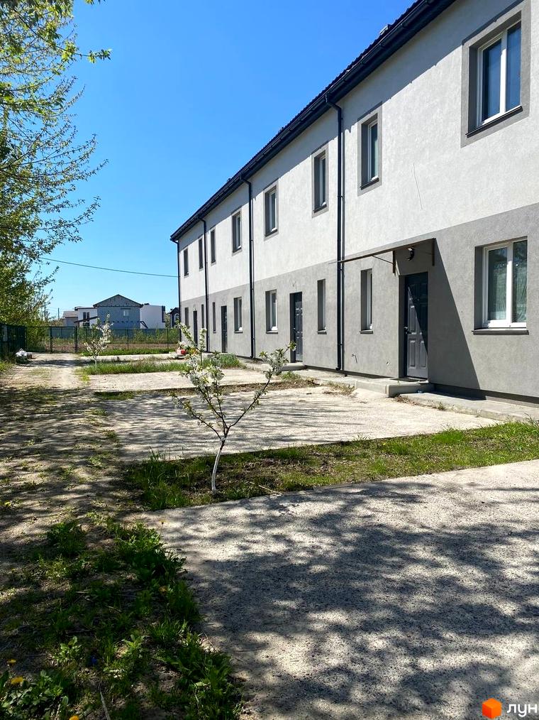 Таунхауси „HarmonyBud“: ряд двоповерхових будинків зі світло-сірими фасадами. Прибудинкова територія має доріжки та молоді дерева.