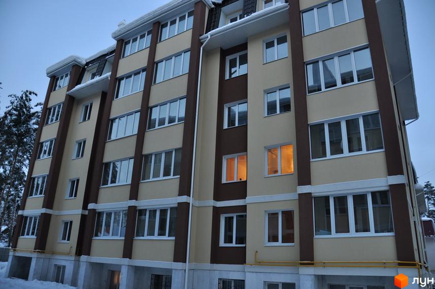 Зовнішній вигляд будинку ЖК Спарта з великими вікнами та балконами. Прибудинкова територія з зеленими насадженнями та снігом.