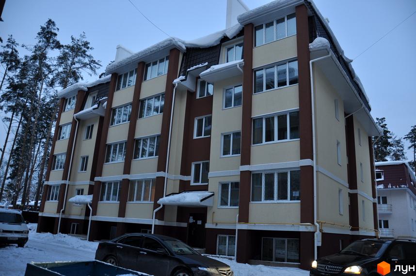 Зовнішній вигляд житлового комплексу ЖК Спарта з чотирьох поверхів, обрамленого деревами. Прибудинкова територія засніжена, з автомобілями на парковці.