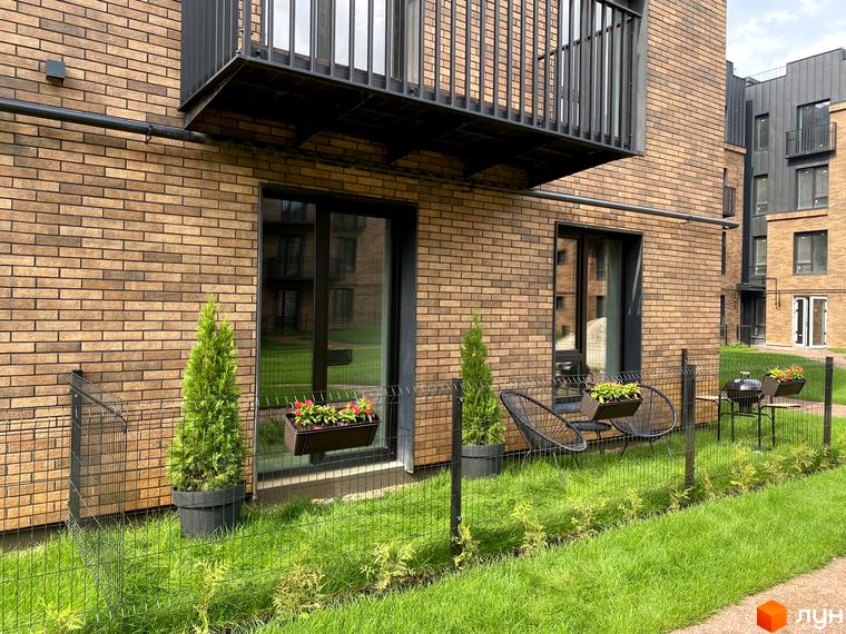 Фасад житлового комплексу Клубне містечко 12 з цегляним оздобленням та балконами. Прибудинкова територія з газоном, огорожею та декоративними рослинами.