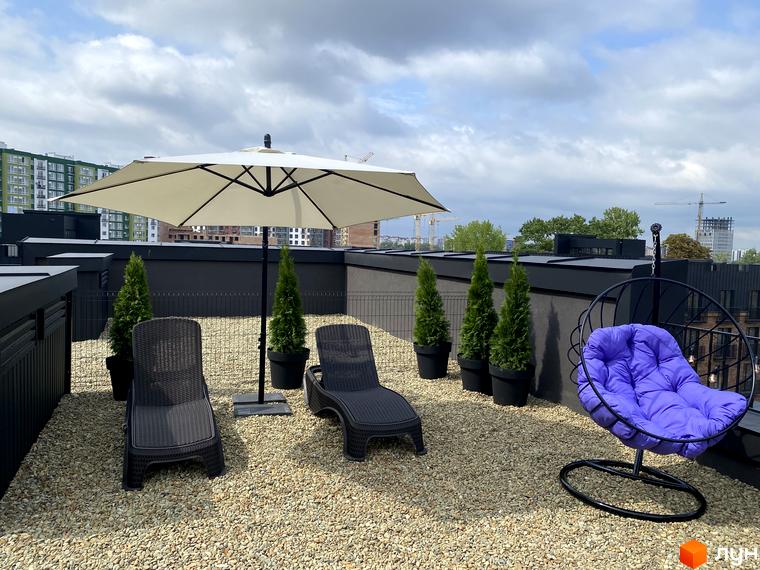 Тераса житлового комплексу Клубне містечко 12 з шезлонгами, парасолькою та підвісним кріслом. На задньому плані видно багатоповерхові будинки та будівельні крани.