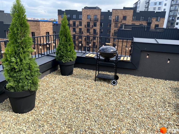 Тераса житлового комплексу Клубне містечко 12 з зеленими туями та грилем. Сучасна новобудова з цегляними фасадами та балконами.