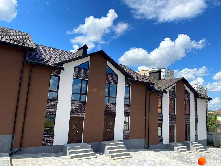 Таунхауси Dream Town 3 з коричневими фасадами, білими акцентами та темними дахами. Перед будинками вимощена бруківка та сходи до входу.