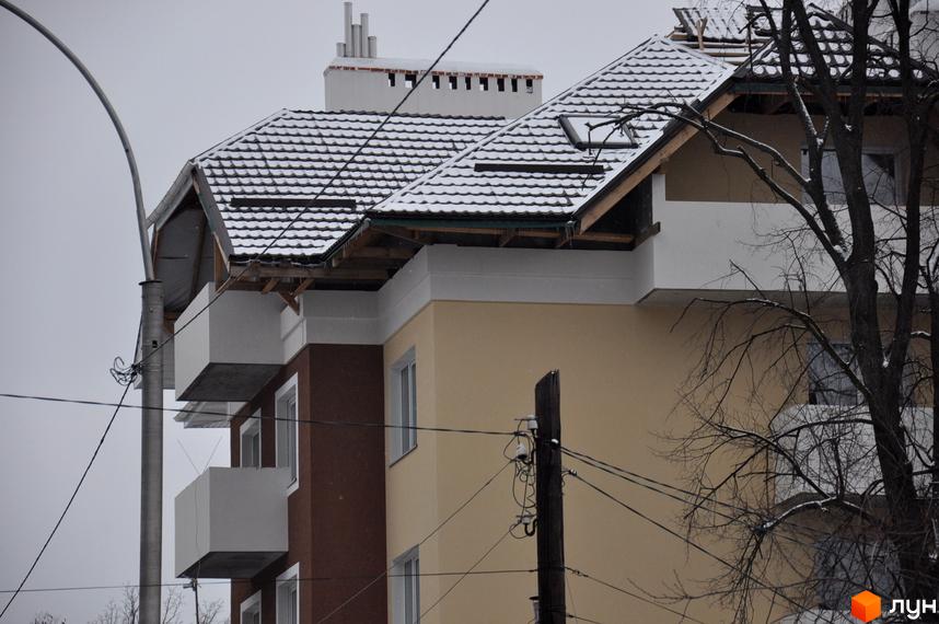 Вигляд новобудови на вул. Університетській, 16 з балконами та покриттям даху. Прибудинкова територія з деревами та електропроводами.