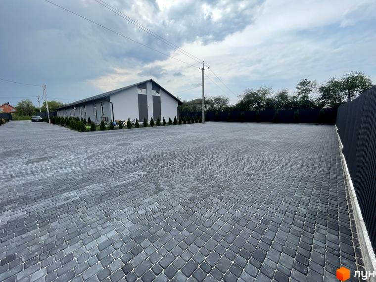 Таунхауси на Мирославській: сіра будівля з темними акцентами та великою брукованою територією.