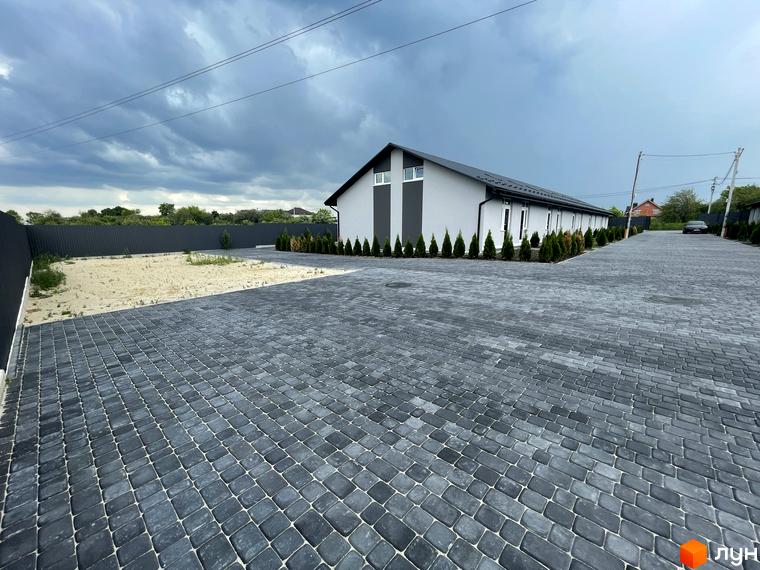 Таунхауси на Мирославській – це двоповерхові будинки сірого кольору з білими вставками, розташовані на брукованій території з акуратно висадженими туями.