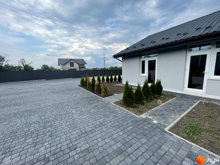 Зовнішній вигляд таунхаусів на Мирославській з сірим фасадом та темним дахом. Прибудинкова територія з бруківкою та зеленими насадженнями.