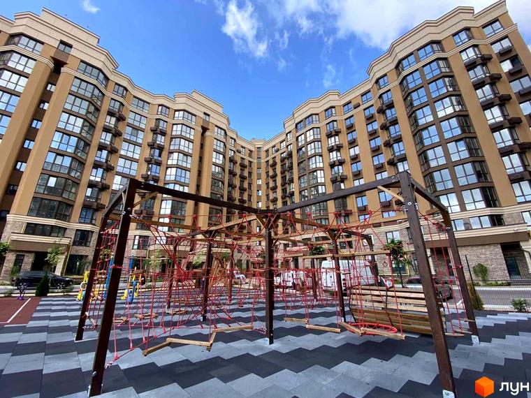 Житловий комплекс Sofia Nova з вигнутими фасадами та великою кількістю вікон. На прибудинковій території розташований сучасний дитячий майданчик з мотузковим містечком.