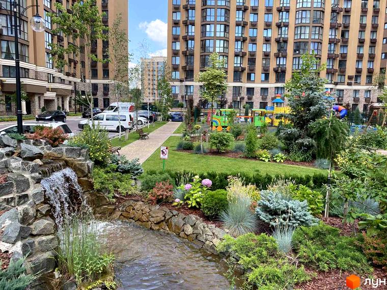 Житловий комплекс Sofia Nova. Зовнішній вигляд будівель та доглянута прибудинкова територія з водоспадом та зеленими насадженнями.