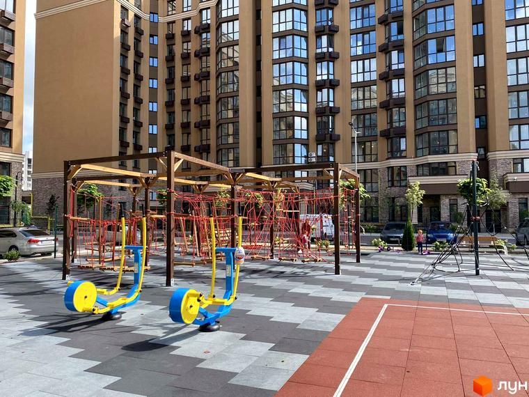 Житловий комплекс Sofia Nova. Сучасний дитячий майданчик та спортивні тренажери на фоні багатоповерхових будинків.