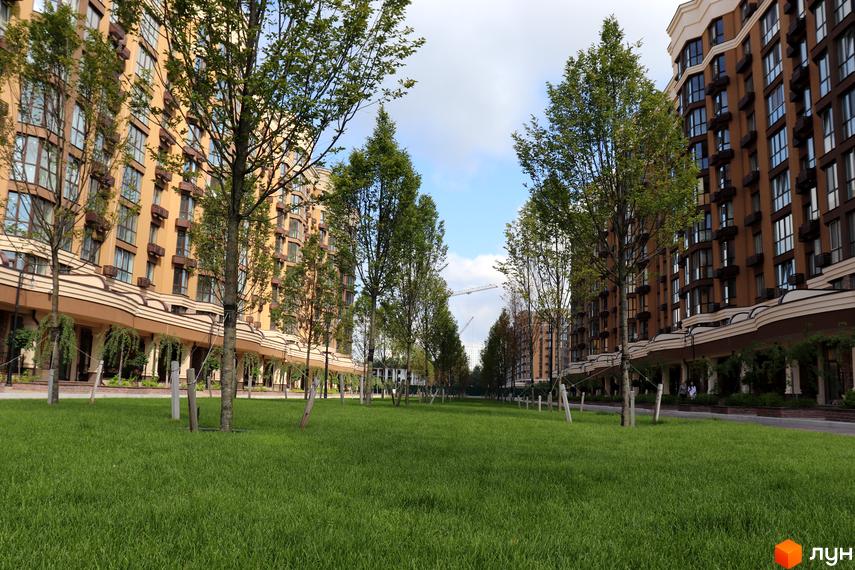 Житловий комплекс Sofia Nova з коричневими та бежевими фасадами, великою кількістю вікон та зеленою прибудинковою територією з деревами.