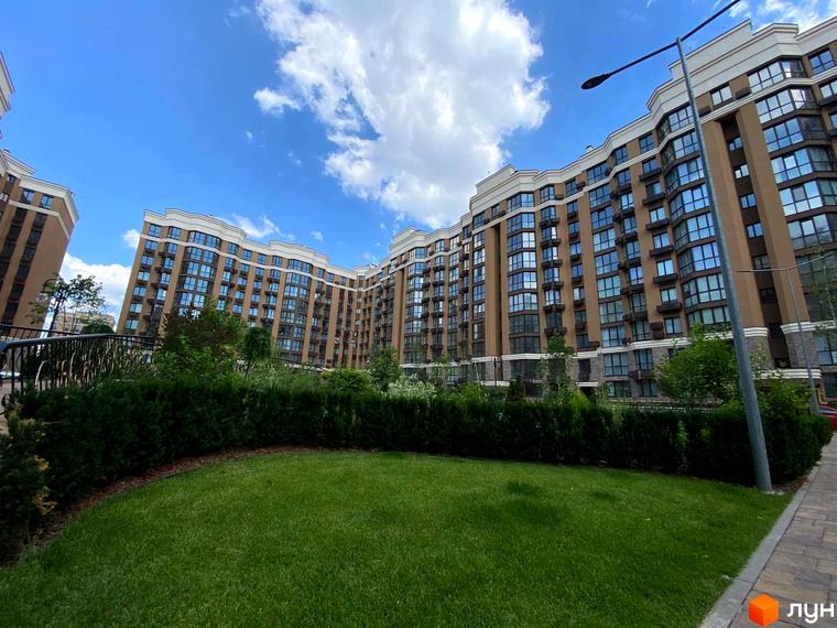 Житловий комплекс Sofia Nova з коричневими фасадами та численними вікнами, що виходить на зелений газон та доглянутий двір з кущами.