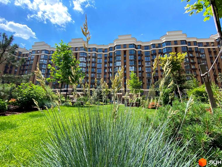 Житловий комплекс Sofia Nova з багатоповерховою будівлею та доглянутою прибудинковою територією з газоном та рослинами. Навколо багато зелені та квітів.