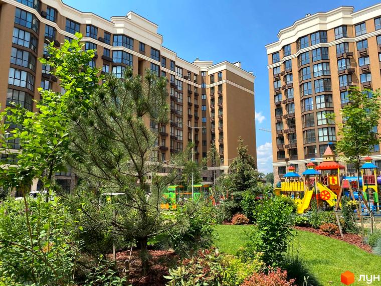 Житловий комплекс Sofia Nova з коричневими фасадами та великою кількістю вікон. На прибудинковій території розташований дитячий майданчик та зелені насадження.