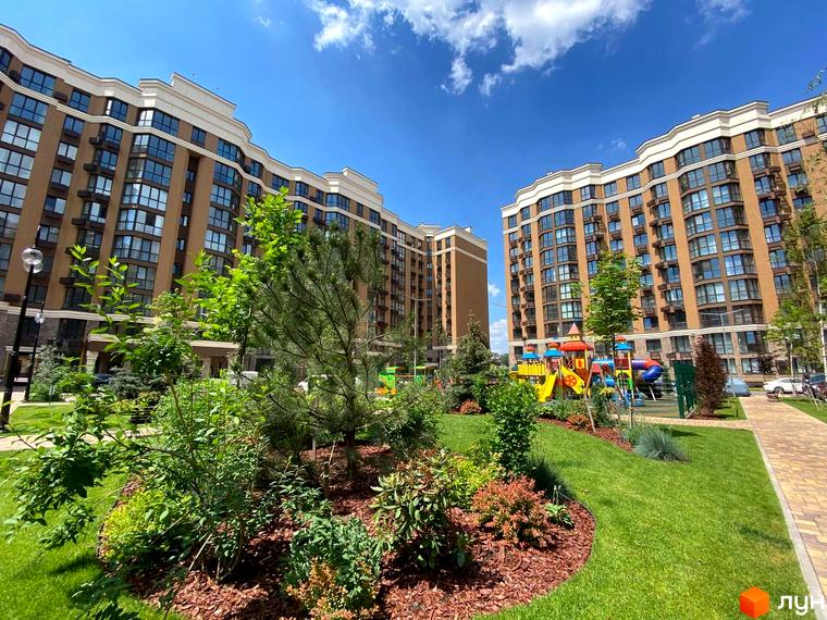 Житловий комплекс Sofia Nova з коричневими фасадами та великими вікнами. Доглянута прибудинкова територія з дитячим майданчиком та зеленими насадженнями.