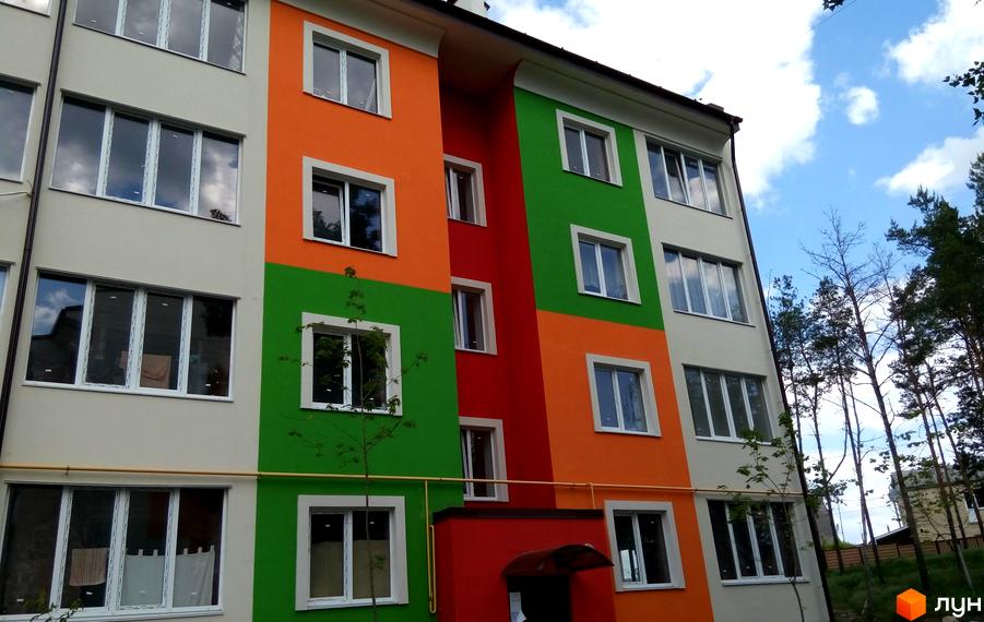 Житловий комплекс Ягода з яскравим фасадом у кольорах оранжевого та зеленого. Прибудинкова територія озеленена молодими деревами.