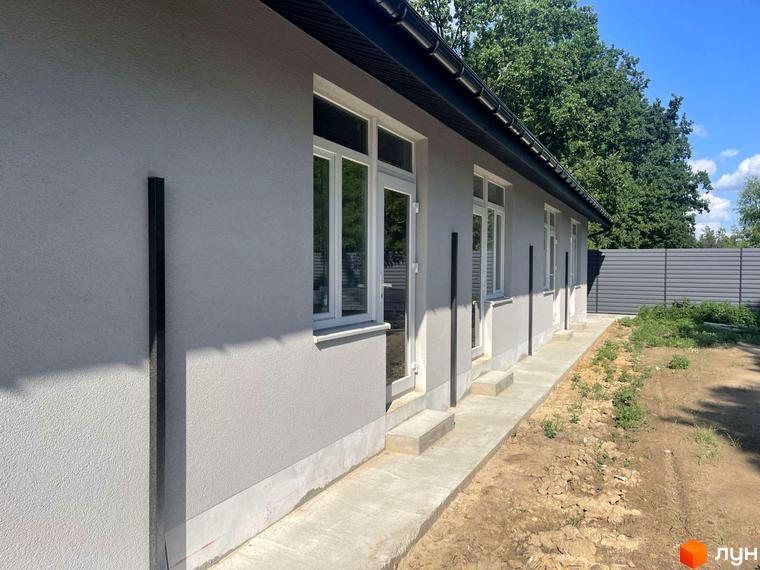 Зовнішній вигляд таунхаусів Оак-Парк з сірим фасадом та білими вікнами, поруч облаштована прибудинкова територія з бетонною доріжкою та зеленими насадженнями.